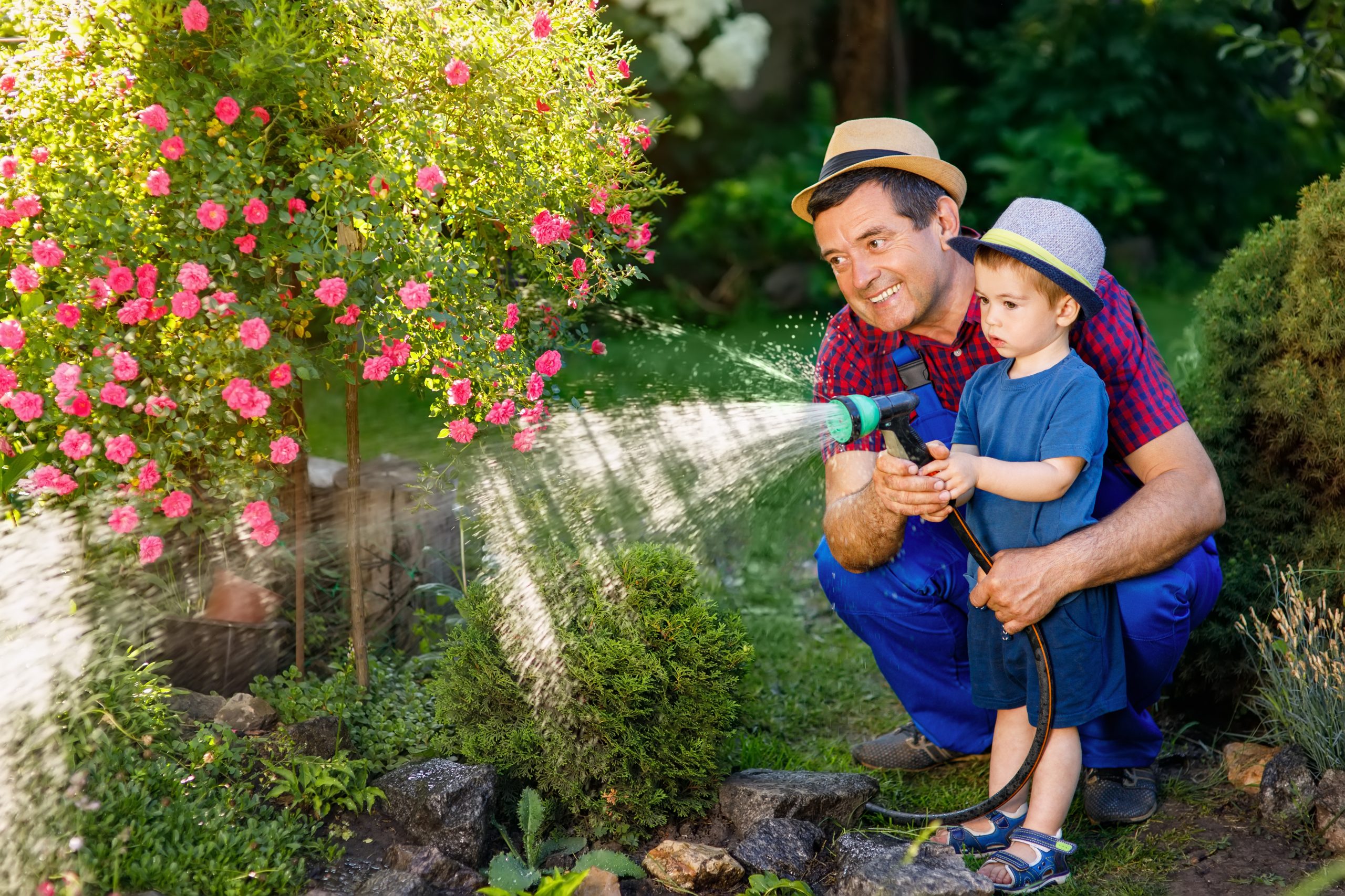 Father and son watering the garden together with steady water pressure — a result of proper pump system maintenance.