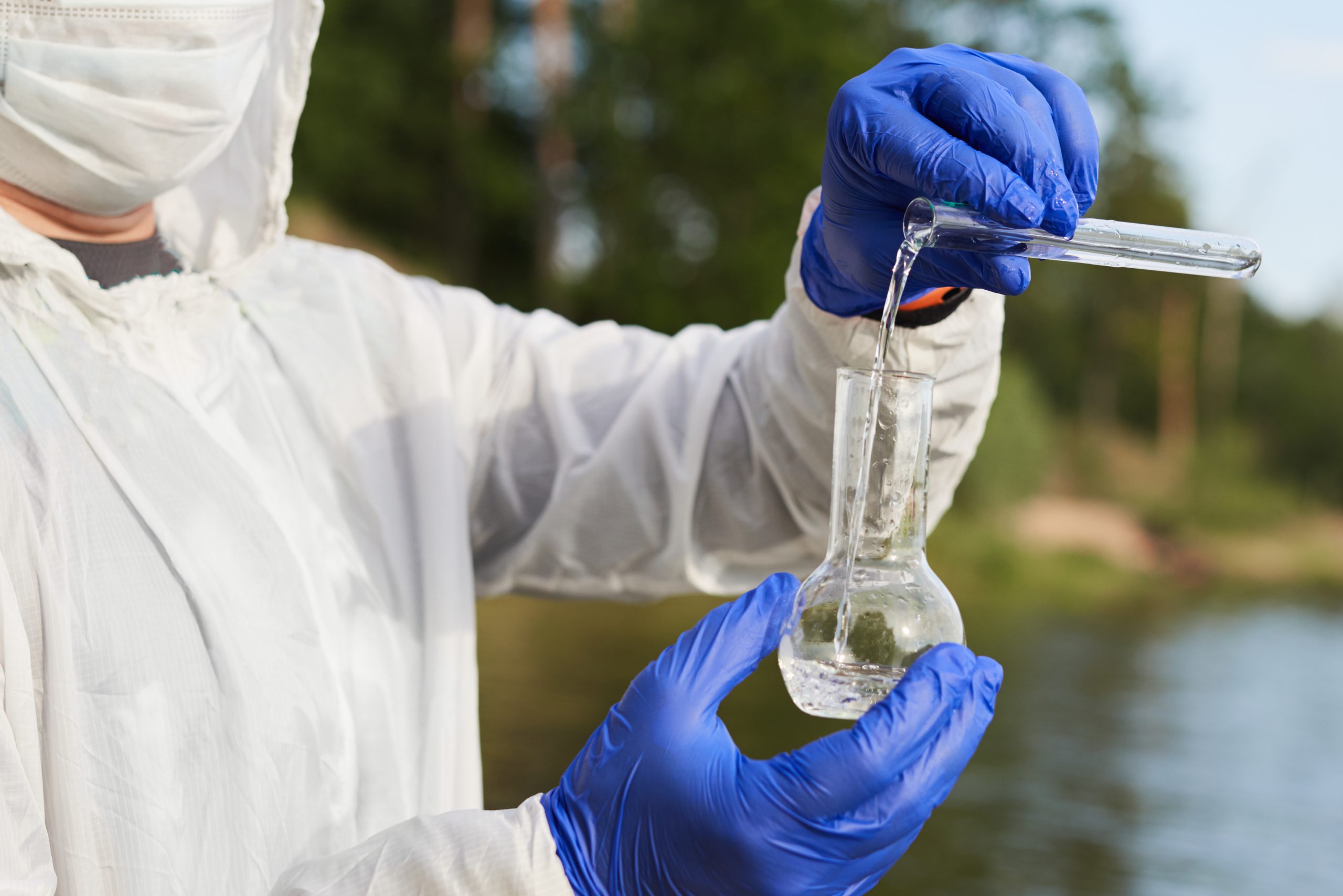water-purity-test-hand-holding-chemical-flask-test-tube-with-water-river-background-scaled