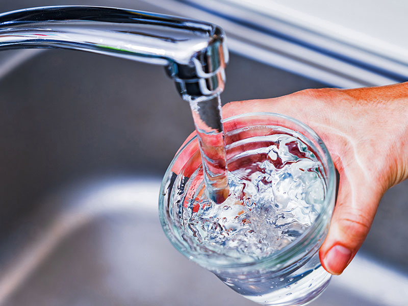 Person filling glass with water from kitchen tap.